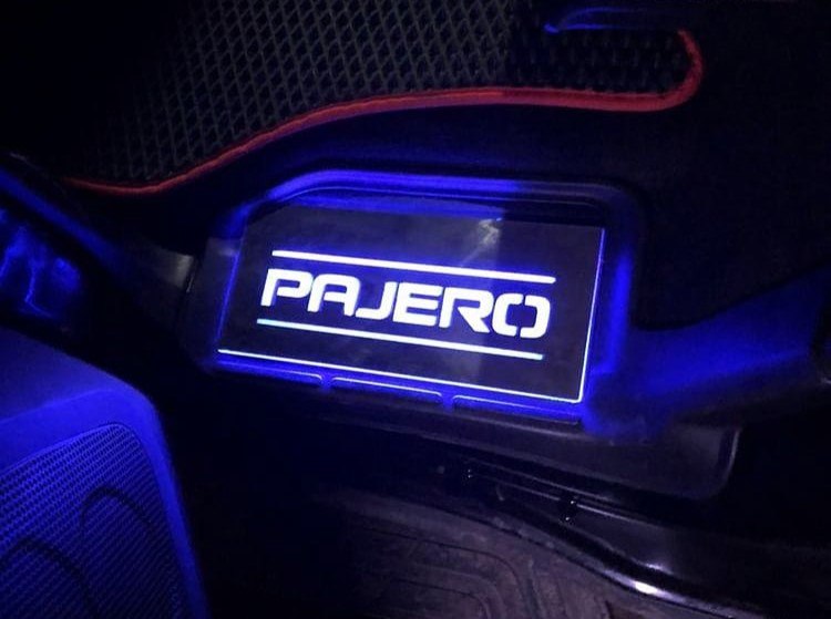 Short rectangular Pajero plate illuminated beside a vehicle floor mat; installation example.