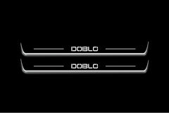 Two long door sill plates with Doblò lettering and edges illuminated in white, straight-on view on a dark background.