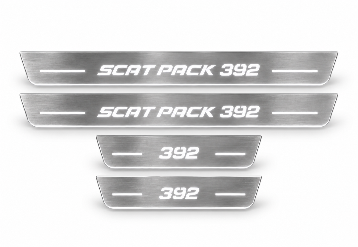 Four brushed stainless Scat Pack 392 door sill plates with white LED lighting on white background.