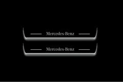 Two long door sill plates with Mercedes-Benz lettering and edges illuminated in white, straight-on view on a dark background.