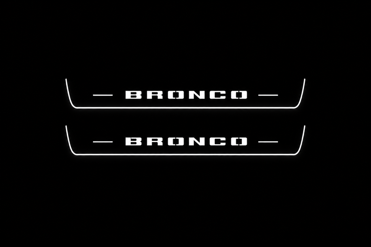Product visualization: two exact short-proportion front plates with original BRONCO stencil letters flat brushed stainless steel door sill plates with white LED artwork and edges, dark background.