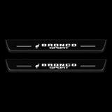 Catalogue illustration of two black Matte PRO front door sill plates with a small horse symbol and stacked illuminated BRONCO SPORT lettering on the top surface. Rear plates are not pictured; dimensions are selected for the vehicle during manufacture.