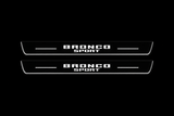 Product visualization: two exact Bronco Sport front plates, stacked original words, no horse flat brushed stainless steel door sill plates with white LED artwork and edges, dark background.