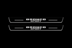 Product visualization: two exact Bronco Sport front plates, stacked original words, no horse flat brushed stainless steel door sill plates with white LED artwork and edges, dark background.