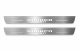 Product visualization: two exact Bronco Sport front plates, stacked original words, no horse flat brushed stainless steel door sill plates with white LED artwork and edges, white background.