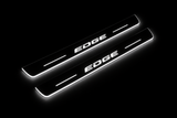 Product visualization: EDGE exact source wordmark, two flat front plates flat brushed stainless steel door sill plates with white LED artwork and edges, dark background.