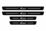 Catalogue illustration of two long front and two shorter rear black Matte PRO door sill plates with illuminated stylized Fiesta lettering and two straight top lines; side and lower edges are unlit. Exact B299 dimensions are selected for the vehicle.