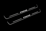 Product visualization: two exact focus-ii-block-diagonal flat Stainless front plates, own source geometry and lettering; hidden night metal, white LED zones flat brushed stainless steel door sill plates with white LED artwork and edges, dark background.