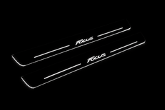 Product visualization: two exact focus-iii-script-diagonal flat Stainless front plates, own source geometry and lettering; hidden night metal, white LED zones flat brushed stainless steel door sill plates with white LED artwork and edges, dark background.