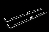 Product visualization: two exact focus-iii-st-diagonal flat Stainless front plates, own source geometry and lettering; hidden night metal, white LED zones flat brushed stainless steel door sill plates with white LED artwork and edges, dark background.