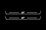 Product visualization: two flat Ford Focus ST front plates with exact ST logo and bars. Black night background, unlit stainless face nearly hidden, white illuminated artwork, bars and real side/end edges with soft glow.
