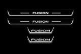 Product visualization: four flat Stainless Steel door-sill plates, two long front and two shorter rear plates. Original artwork and actual edge/end LED zones illuminated white on black; not an installation photograph.