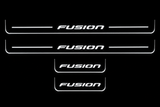 Product visualization: four original flat Fusion sill plates, two front with bars and two shorter rear without bars; white illumination flat brushed stainless steel door sill plates with white LED artwork and edges, dark background.