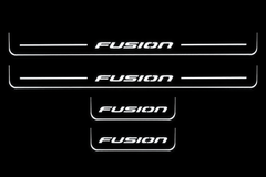 Product visualization: four original flat Fusion sill plates, two front with bars and two shorter rear without bars; white illumination flat brushed stainless steel door sill plates with white LED artwork and edges, dark background.