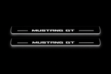 Product visualization: mustang-gt-s197 exact MUSTANG GT source artwork, two flat front plates flat brushed stainless steel door sill plates with white LED artwork and edges, dark background.