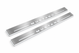 Product visualization: MUSTANG spaced letters, two flat source front plates flat brushed stainless steel door sill plates with white LED artwork and edges, white background.