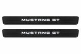 Catalogue illustration of two black Matte PRO front sill plates with illuminated MUSTANG GT lettering on top. Decorative bars and edges remain unlit; no rear plates or exact dimensions pictured.