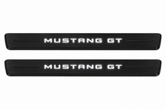 Catalogue illustration of two black Matte PRO front sill plates with illuminated MUSTANG GT lettering on top. Decorative bars and edges remain unlit; no rear plates or exact dimensions pictured.