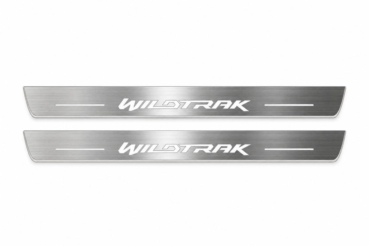 Product visualization: two flat front plates with original italic WILDTRAK logo and side bars flat brushed stainless steel door sill plates with white LED artwork and edges, white background.