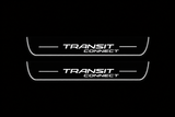 Product visualization: two flat front plates with original TRANSIT over CONNECT two-line logo and side bars flat brushed stainless steel door sill plates with white LED artwork and edges, dark background.