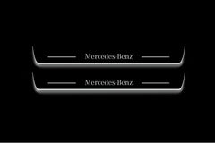 Two long door sill plates with Mercedes-Benz lettering and edges illuminated in white, straight-on view on a dark background.