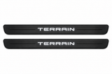 Catalogue illustration of two black Matte PRO front door sill plates with illuminated TERRAIN lettering on the upper surface. One decorative line on each side remains unlit; rear plates for FRONT+REAR are not pictured. Dimensions are selected for GMC Terrain II C1 during manufacture.