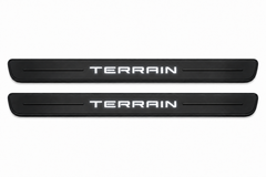 Catalogue illustration of two black Matte PRO front door sill plates with illuminated TERRAIN lettering on the upper surface. One decorative line on each side remains unlit; rear plates for FRONT+REAR are not pictured. Dimensions are selected for GMC Terrain II C1 during manufacture.