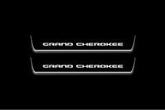 Two short door sill plates with Grand Cherokee lettering and edges illuminated in white, straight-on view on a dark background.