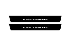 Catalog illustration of two black front door sill plates with Grand Cherokee lettering.