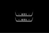 Two short door sill plates with GTI lettering and edges illuminated in white, straight-on view on a dark background.