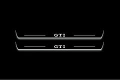 Two long door sill plates with GTI lettering and edges illuminated in white, straight-on view on a dark background.