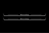 Two long door sill plates with Hennessey lettering and edges illuminated in white, straight-on view on a dark background.