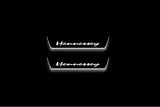Two short door sill plates with Hennessey lettering and edges illuminated in white, straight-on view on a dark background.