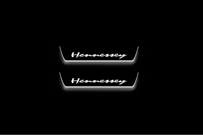Two short door sill plates with Hennessey lettering and edges illuminated in white, straight-on view on a dark background.