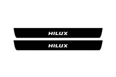 Catalog illustration of two black front door sill plates with Hilux lettering.