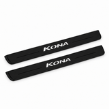 Catalogue illustration of two black Matte PRO front door sill plates with illuminated KONA lettering on the top surface. Edges are unlit; rear plates for FRONT+REAR are not pictured. Final dimensions are selected for Hyundai Kona OS during manufacture.