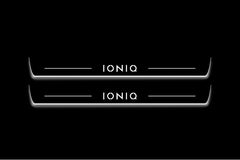 Two long door sill plates with Ioniq lettering and edges illuminated in white, straight-on view on a dark background.