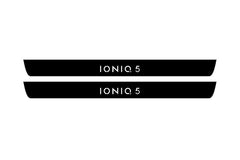 Catalog illustration of two black front door sill plates with Ioniq 5 lettering.