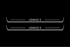 Two long door sill plates with IONIQ 5 lettering and edges illuminated in white, straight-on view on a dark background.