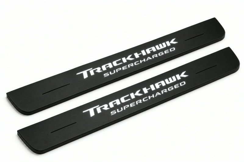 Catalogue illustration of two front black Matte PRO LED door sill plates with illuminated TrackHawk Supercharged lettering for Jeep Grand Cherokee WK2; dimensions are selected during manufacture.