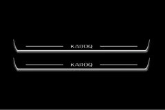 Two long door sill plates with Karoq lettering and edges illuminated in white, straight-on view on a dark background.