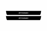Catalogue illustration of two black Matte PRO front door sill plates with white illuminated Stonic lettering. The FRONT+REAR option also includes two rear plates not pictured; final dimensions are selected for the vehicle during manufacture.