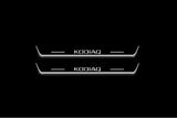 Two short door sill plates with Kodiaq lettering and edges illuminated in white, straight-on view on a dark background.