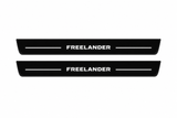 Catalogue illustration of two front black Matte PRO LED door sill plates with illuminated Freelander lettering for Land Rover Freelander 2 L359; the FRONT+REAR option includes rear plates not shown; final dimensions are selected during manufacture.