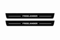 Catalogue illustration of two front black Matte PRO LED door sill plates with illuminated Freelander lettering for Land Rover Freelander 2 L359; the FRONT+REAR option includes rear plates not shown; final dimensions are selected during manufacture.