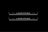 Two long door sill plates with Landtrek lettering and edges illuminated in white, straight-on view on a dark background.
