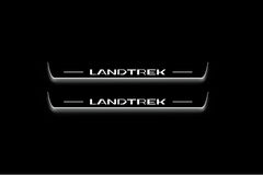Two long door sill plates with Landtrek lettering and edges illuminated in white, straight-on view on a dark background.