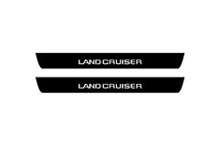 Catalog illustration of two black front door sill plates with Land Cruiser lettering.