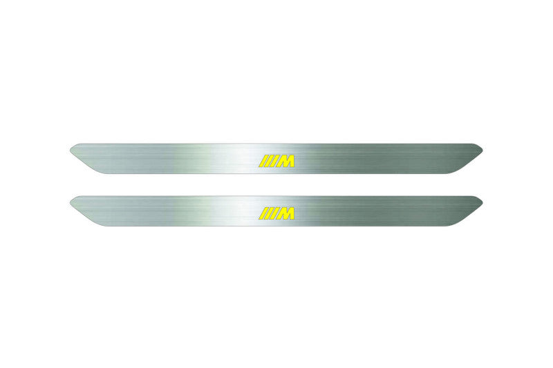 Catalog illustration of two narrow silver door sill inserts with yellow striped M emblems on a white background.