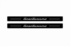 Catalogue demonstration of two black Matte PRO front sill plates with illuminated GranTurismo script and straight top lines. No rear plates are included or pictured; M145 dimensions are selected during manufacture.
